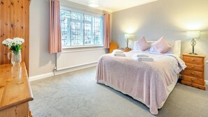 Une chambre avec une grande fenêtre, un lit avec une literie rose, deux tables de chevet avec des lampes et une commode en bois.