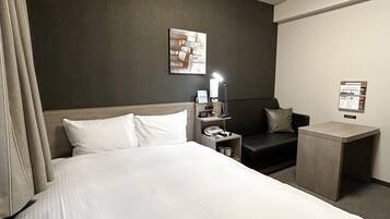 Una habitación de hotel con una cama grande, un escritorio, una silla, una lámpara y un armario pequeño.