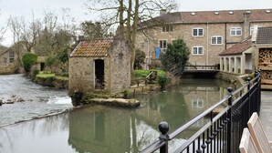 A stone bridge over a calm river, with stone buildings and a small wooden structure on the riverbank. - 3 bedroom accommodation in Spring Gardens, Frome (Spring Gardens, Frome)