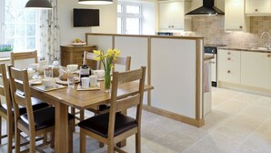 A modern kitchen with a dining area, featuring a wooden table, chairs, and a vase of flowers. - 3 bedroom accommodation in Spring Gardens, Frome (Spring Gardens, Frome)