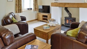 A cozy living room with leather sofas, a wooden coffee table, a television, and a wood-burning stove. - 3 bedroom accommodation in Spring Gardens, Frome (Spring Gardens, Frome)