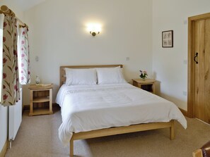 A neatly made bed with white linens, a bedside table with a vase of flowers, and a wall-mounted light fixture. - 3 bedroom accommodation in Spring Gardens, Frome (Spring Gardens, Frome)