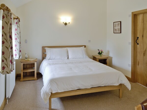 A neatly made bed with white linens, a bedside table with a vase of flowers, and a wall-mounted light fixture.