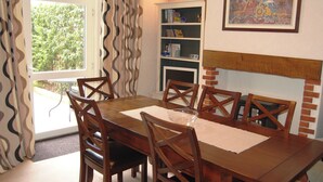 Een eethoek met een houten tafel en stoelen, een boekenkast, een open haard en een raam met gordijnen.