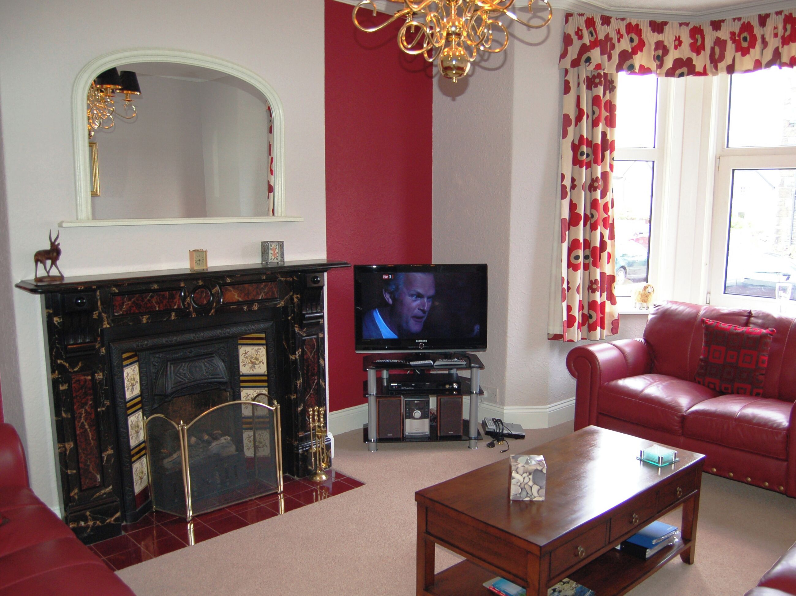 A living room with a fireplace, a television, a red sofa, and a chandelier.
