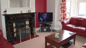 Een woonkamer met een open haard, een televisie, een rode bank en een kroonluchter.