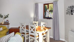 Un coin repas avec une table et des chaises en bois, une fenêtre avec des rideaux, une petite plante et un radiateur.
