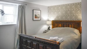 Une chambre à coucher avec un lit en bois, une fenêtre avec des rideaux, une lampe fixée au mur et un tableau encadré.