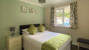 A bedroom with a bed, bedside tables, a bench, a window with curtains, and wall art. - 3 bedroom accommodation in Liskeard (Liskeard)