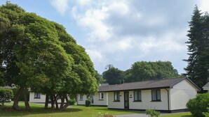 A single-story building with a flat roof, surrounded by well-maintained grass and trees. - 3 bedroom accommodation in Liskeard (Liskeard)