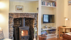 Ein gemütliches Wohnzimmer mit Kamin aus Stein, einem Flachbildfernseher, einem Bücherregal und einem Ledersofa.