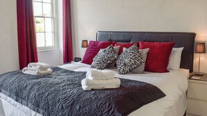 Ein ordentlich bezogenes Bett mit einer schwarz-weißen Steudecke, roten und schwarzen Kissen und weißen Handtüchern.