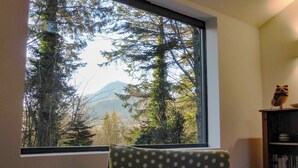 Ein Zimmer mit großem Fenster, einem Sessel und einem Bücherregal.