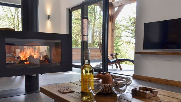 Ein modernes Interieur mit Kamin, einer Weinflasche, Gläsern und einem Fernseher auf einem Holztisch.