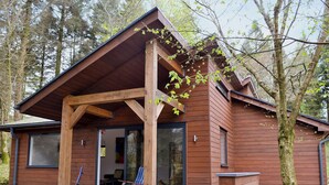 Eine Holzhütte mit überdachter Veranda, Glastür und zwei Liegestühlen vor der Tür.
