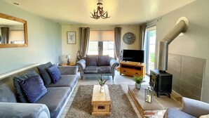 A living room with a sofa, armchairs, a coffee table, a TV, a fireplace, and a clock on the wall.