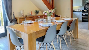 A dining room with a wooden table set for six, grey chairs, a vase with flowers, and a staircase with wooden railings.