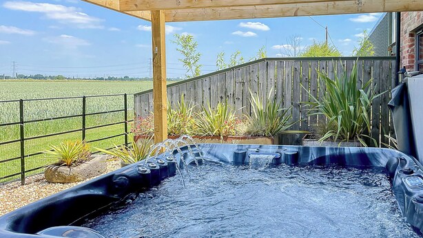 A hot tub under a wooden pergola with a view of a fenced field.