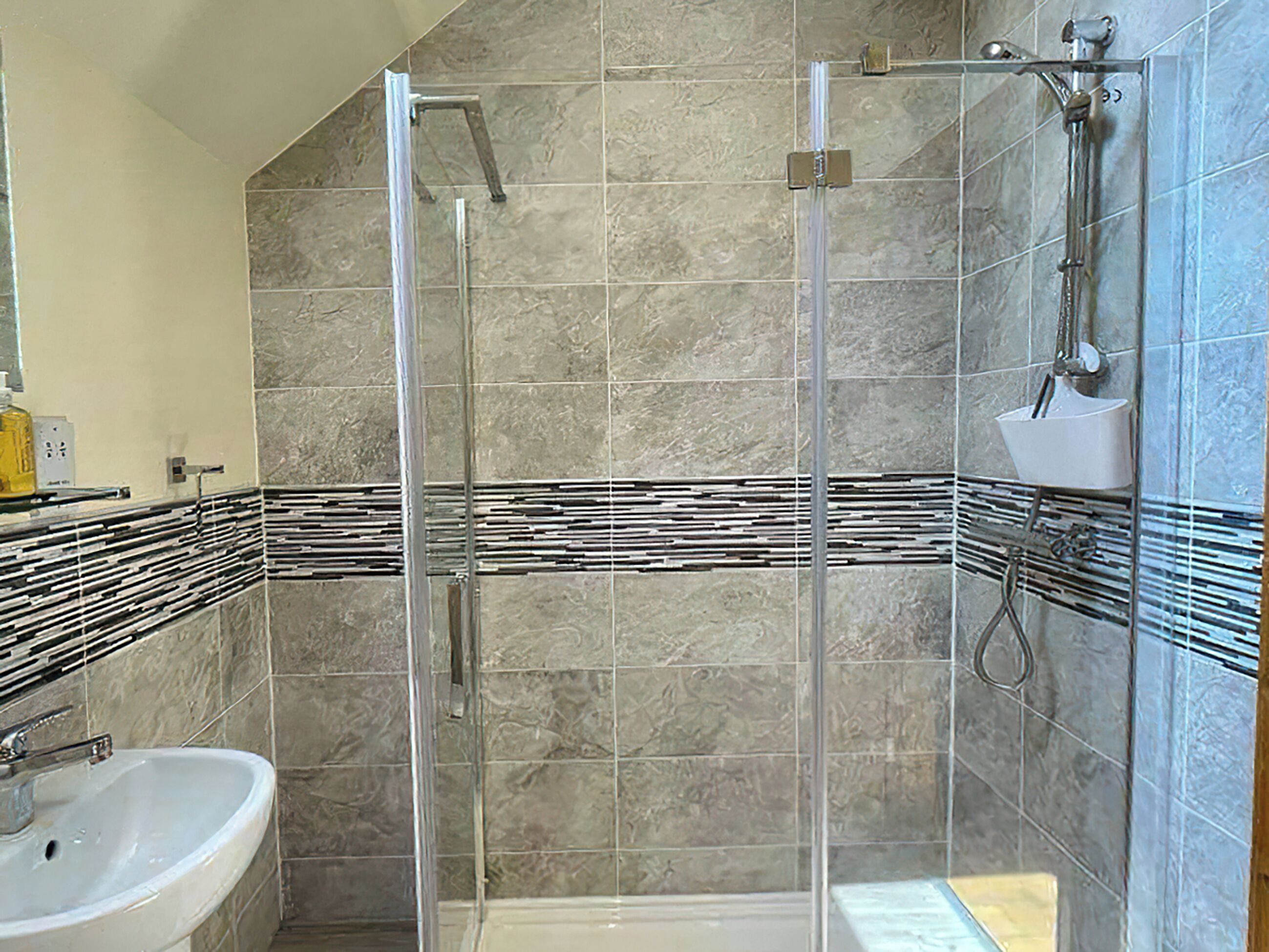 Une salle de bain avec une douche à parois de verre, un lavabo et un mur carrelé agrémenté d’une bordure décorative.