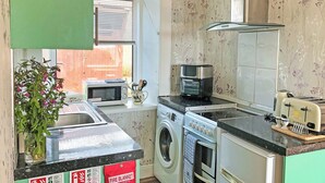 A compact kitchen with a washing machine, microwave, toaster, and a fire blanket sign. - Old Barn Farm Cottage - CC539048 (Uplawmoor, near Paisley)