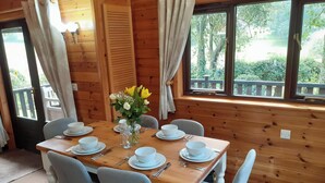 A wooden dining room with a table set for four, chairs, and a vase with flowers. - Ewe How - Burnside Park (Keswick)