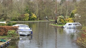 Ein ruhiger Fluss mit anlegenden Booten am Ufer, umgeben von Bäumen und Grün.