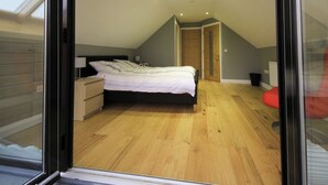 Ein Schlafzimmer mit Bett, Nachttisch, Lampe und Blick auf einen Flur.