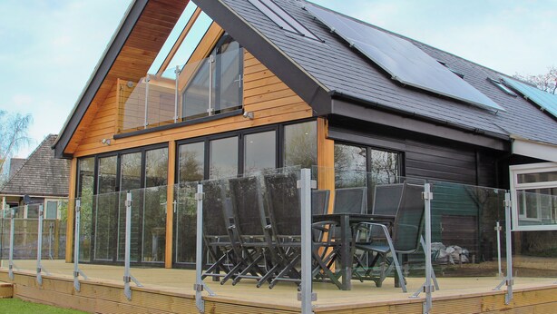 Ein modernes Haus mit großem Glasanbau, geneigtem Dach und einer Holzterrasse.