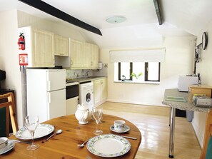 A kitchen with wooden cabinets, a washing machine, a dining table set with plates, glasses, and cutlery. - Rosecraddoc Manor - Hayloft (Near Liskeard)