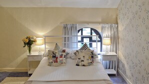 Une chambre à coucher bien rangée, avec un lit, deux tables de chevet, une fenêtre avec des rideaux et un papier peint à motifs floraux.
