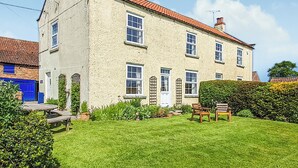 A two-story house with a red-tiled roof, a well-maintained lawn, and a wooden bench in the front yard. - Foston Grange Cottage (Foston near York)