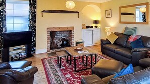 A living room with a fireplace, leather sofas, a coffee table, and a red patterned rug. - Foston Grange Cottage (Foston near York)