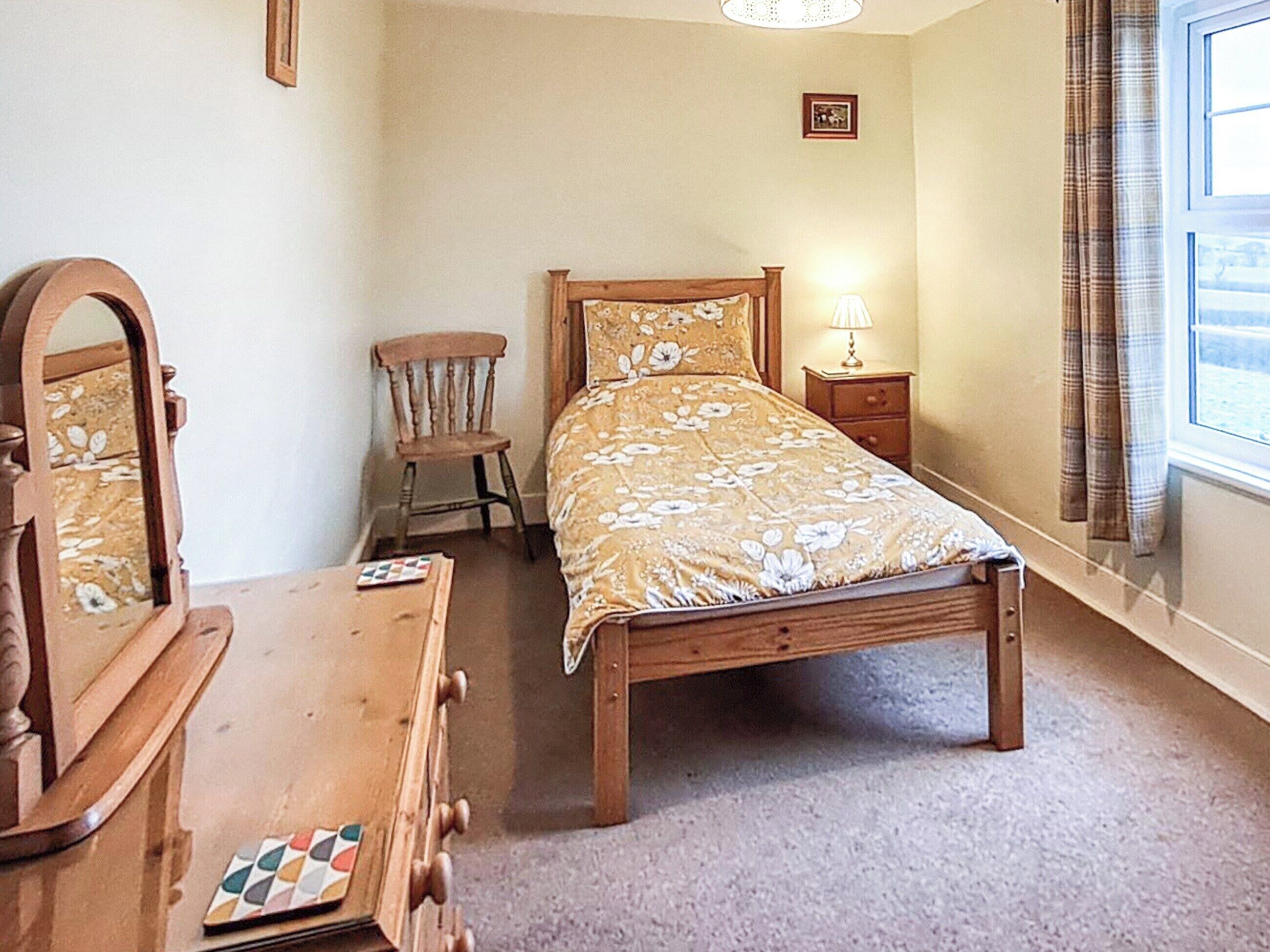 Quarto com cama de madeira, uma cadeira, cômoda e espelho.