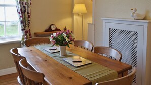 A dining area with a wooden table, chairs, a vase with flowers, a lamp, and a fireplace with a decorative swan. - Foston Grange Cottage (Foston near York)