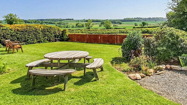 A picnic table with benches in a grassy outdoor area with a view of rolling hills. - Foston Grange Cottage (Foston near York)