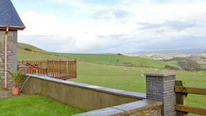 Un bâtiment en pierre doté d’une terrasse en bois qui donne sur un champ verdoyant où paissent des moutons.