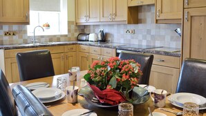 Une cuisine moderne avec des meubles en bois, un plan de travail en granit et un coin repas aménagé pour quatre personnes, avec une table, des chaises et un vase de fleurs.