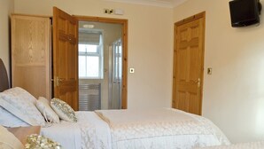 Une chambre avec deux lits, des portes en bois, un espace douche et un téléviseur fixé au mur.