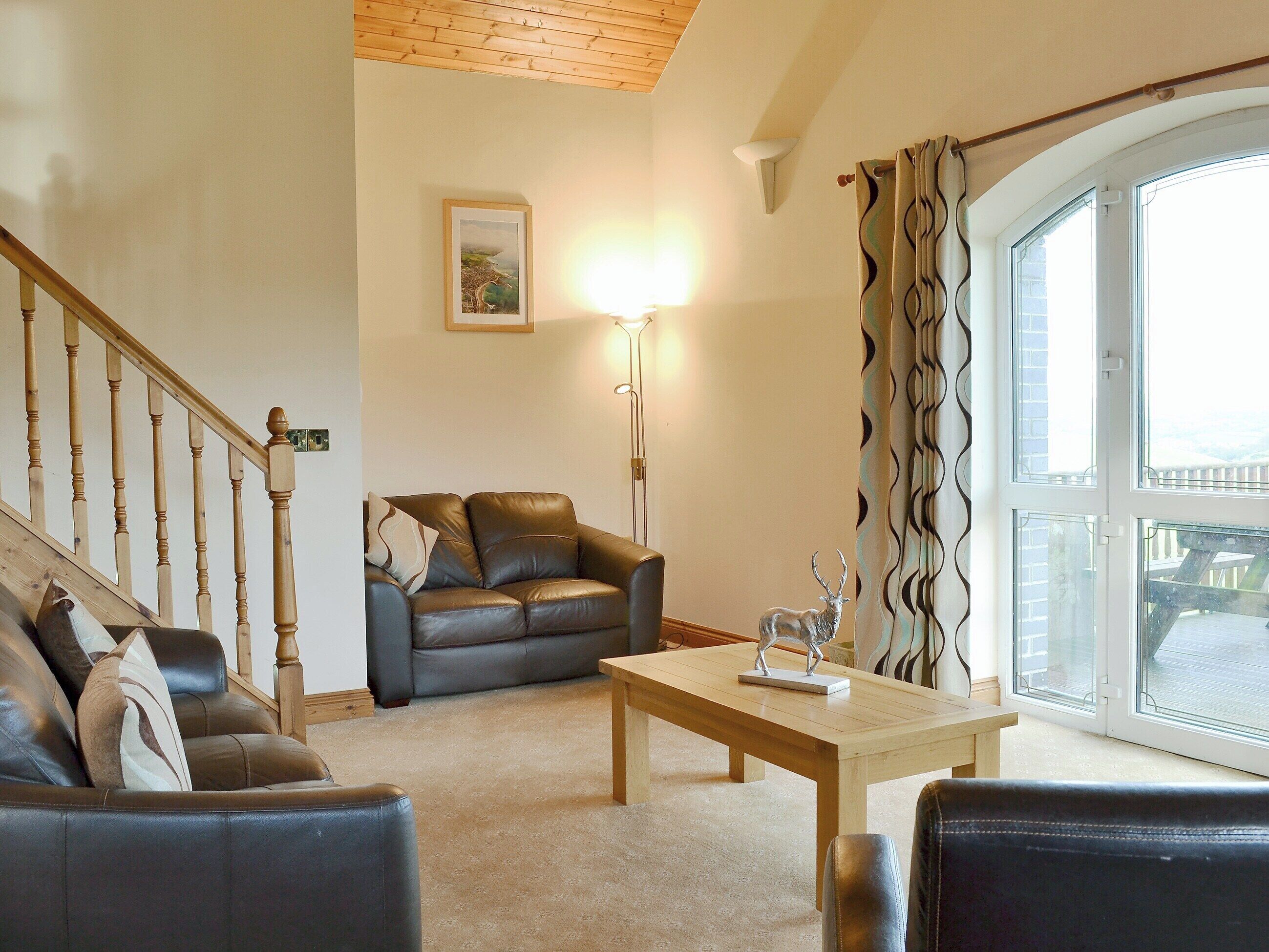 A living room with a brown leather sofa, a wooden coffee table, and a staircase with wooden railings.