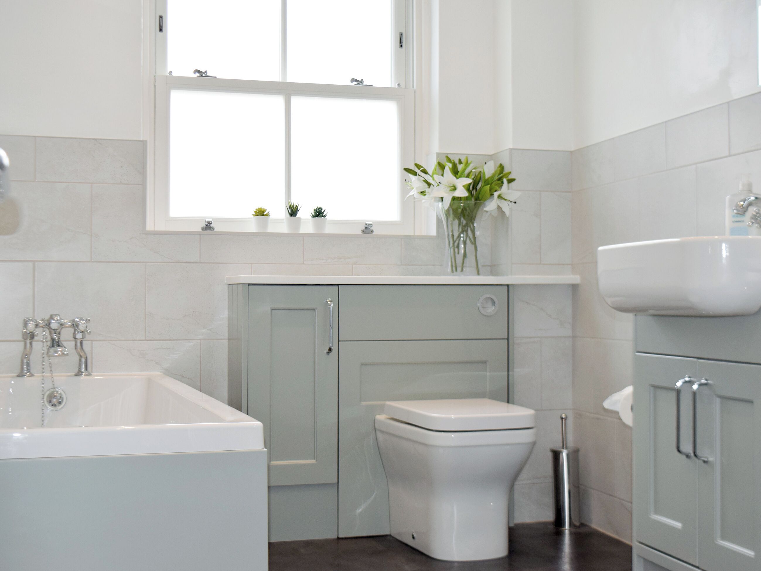 A bathroom with a bathtub, toilet, sink, and a window with plants on the windowsill.