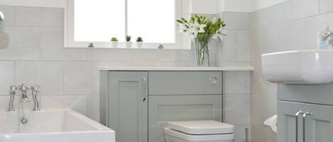 A bathroom with a bathtub, toilet, sink, and a window with plants on the windowsill.