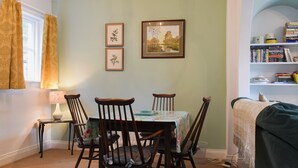Un coin repas comprenant une table, des chaises, une lampe, des tableaux encadrés et une bibliothèque.
