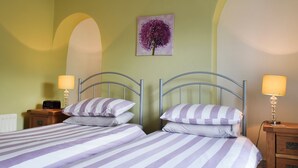 Un lit double avec une literie à rayures, deux tables de chevet avec des lampes, un tableau accroché au mur et un radiateur.