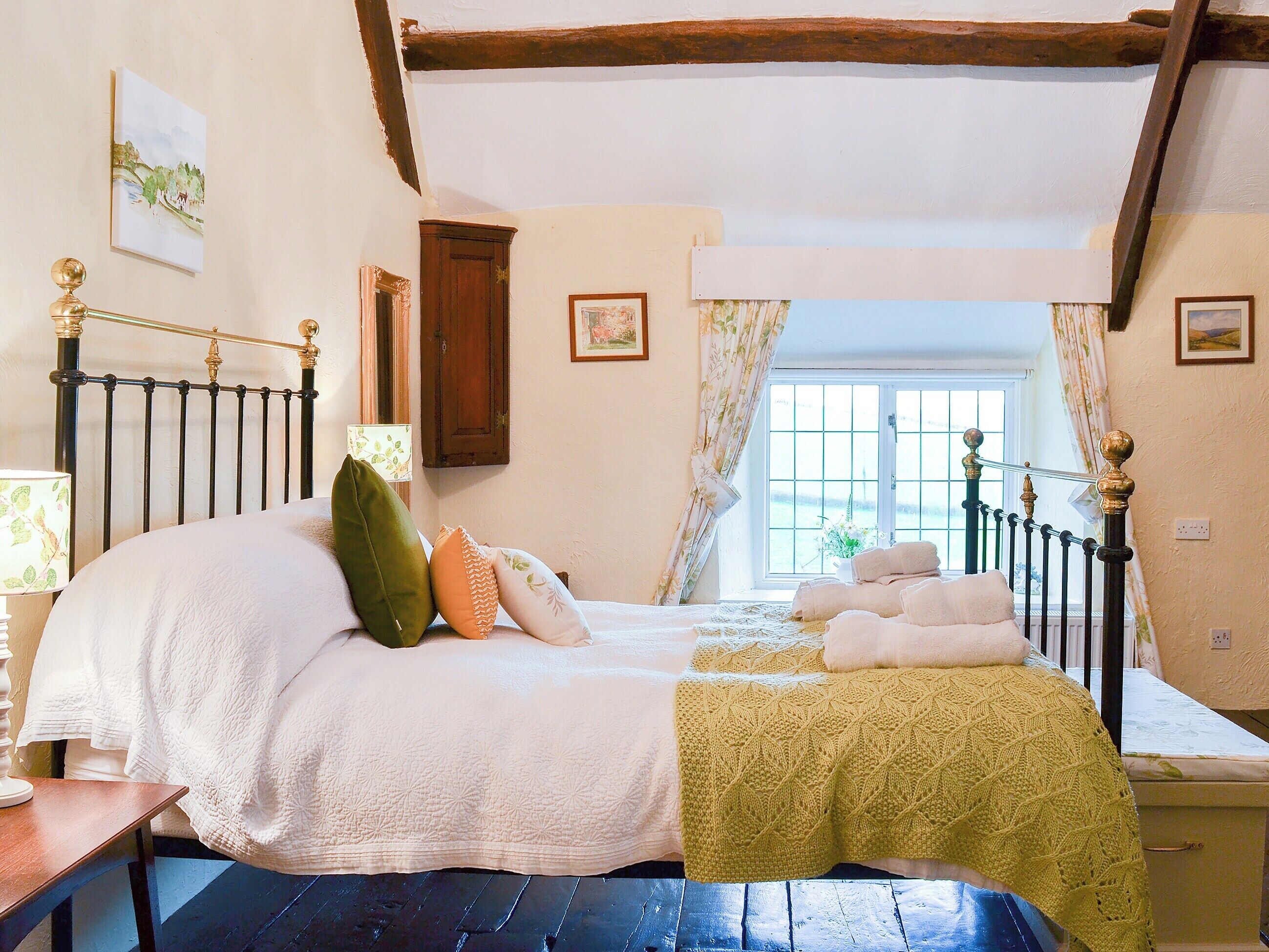 A bedroom with a bed, a nightstand, a window with curtains, and a wooden ceiling.