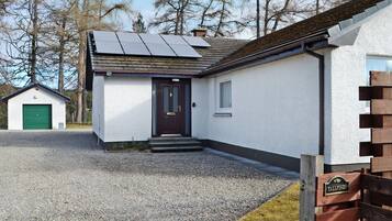 A house with a gravel driveway, a green garage door, a dark front door, and solar panels on the roof.