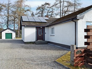 A house with a gravel driveway, a green garage door, a dark front door, and solar panels on the roof. - 4 bedroom accommodation in Carrbridge (Carrbridge)