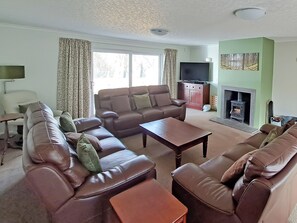 A living room with leather sofas, a coffee table, a flat-screen TV, and a fireplace. - 4 bedroom accommodation in Carrbridge (Carrbridge)