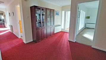 A hallway with a red carpet, a wooden cabinet with glass doors, and a door leading to another room.