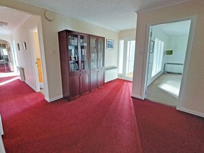A hallway with a red carpet, a wooden cabinet with glass doors, and a door leading to another room. - 4 bedroom accommodation in Carrbridge (Carrbridge)