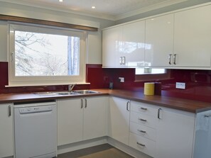 A kitchen with white cabinets, a dishwasher, a window with a view of trees, and a red backsplash. - 4 bedroom accommodation in Carrbridge (Carrbridge)